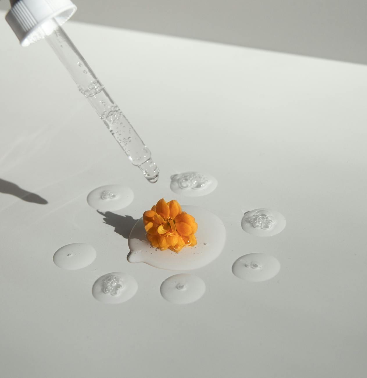 pipette with transparent essence and yellow flower on white surface