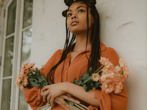 woman wearing box braids holding bouquet of flowers leaning against wall