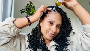 Black woman with box braids applying Herb Infused Hair Oil