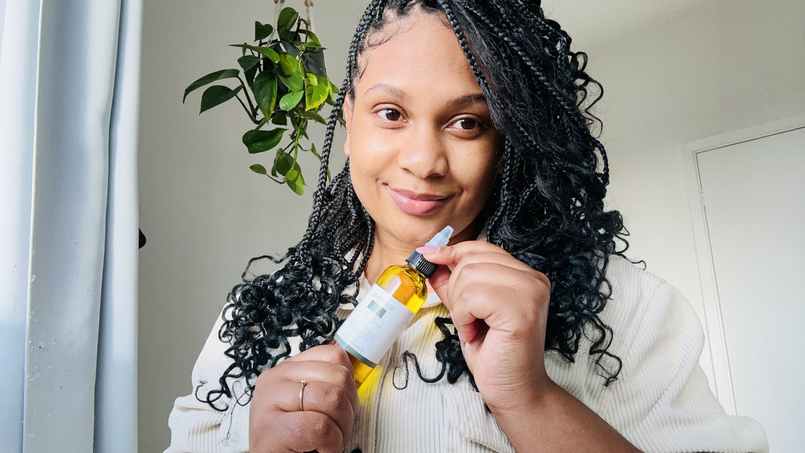 Black woman with box braids holding Herb Infused Hair Oil